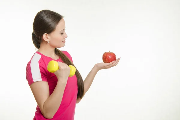 Sportowiec trzęsie mięśnie prawej ręki hantle i patrząc na jabłka w lewej ręce — Zdjęcie stockowe