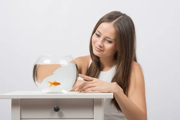 Ze klopt op de vinger op het glas aquarium met goudvis — Stockfoto