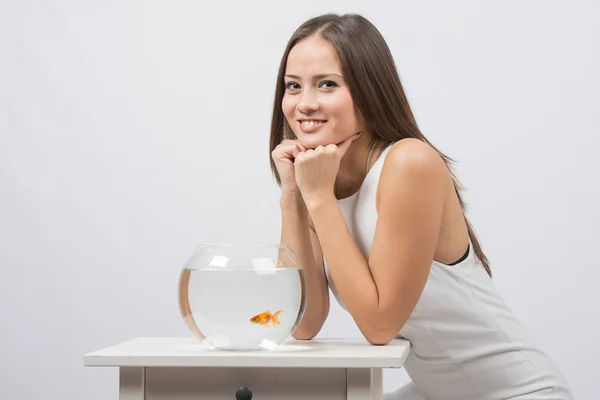 La fille est assise près de l'aquarium avec des poissons rouges et regarde dans l'image — Photo