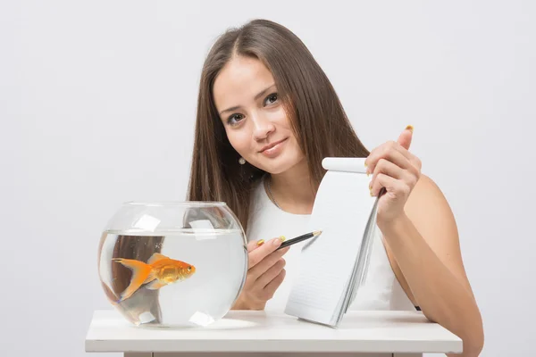 Girl shows a pen in a notebook record gold fish in the aquarium — Stock Photo, Image