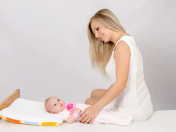 Mãe feliz sentada em uma cama e olhando para uma filha de dois meses — Fotografia de Stock