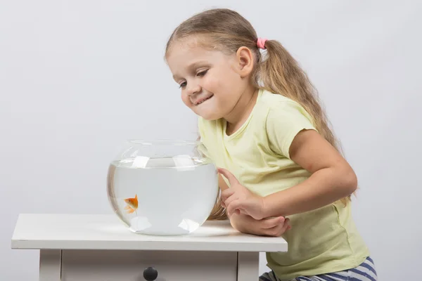 Vierjarig meisje glimlachend kijken naar een goudvis in een aquarium — Stockfoto