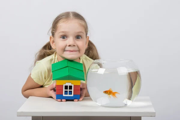 Четырехлетняя девочка держит игрушечный домик и сидит перед золотой рыбкой — стоковое фото