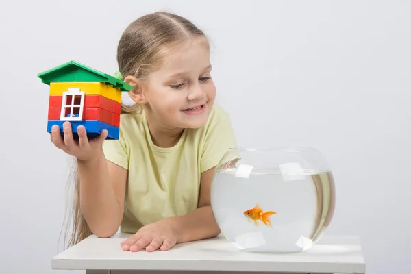 Четырехлетняя девочка сидит с игрушечным домиком перед золотой рыбкой — стоковое фото