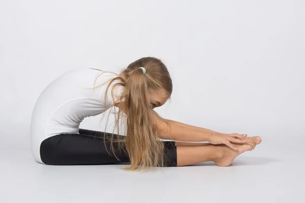 Chica gimnasta realiza un pliegue sentado en el suelo tira de las manos a los dedos de los pies — Foto de Stock