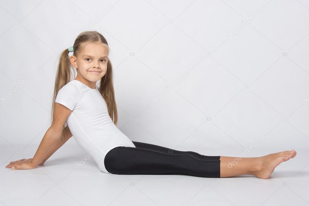 Girl gymnast sitting on the floor with legs stretched and leaned back on his hands