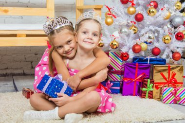 Girl hugging another girl sitting on a mat at the Christmas tree