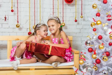 Girl whispering a secret that some other girl sitting on a bench with a Christmas present
