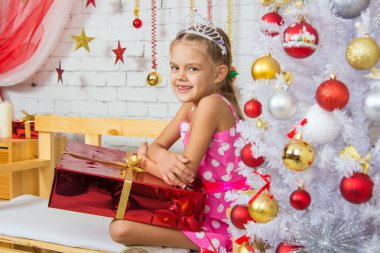 Smiling girl sitting on a bench with a huge gift from the Christmas trees