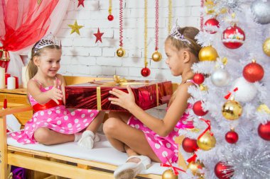 Girl gives a big red Christmas gift another girl sitting on the bench