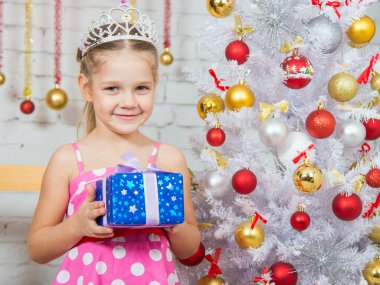  Girl holding a Christmas gift and standing near Christmas trees