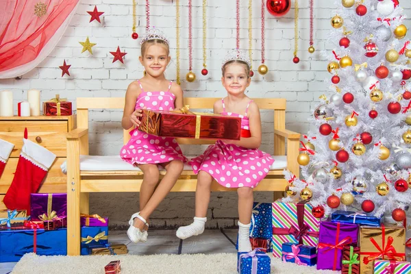 Happy sisters holding a big red gift and sit on a bench in a Christmas setting — Stockfoto