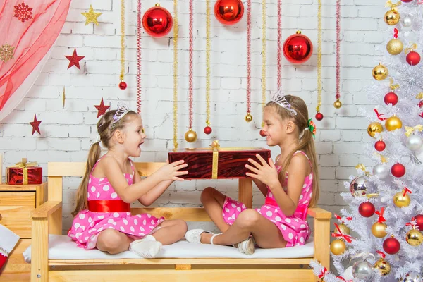 Chicas sentadas en un banco en un ambiente de Navidad y mantener el gran regalo rojo en las manos — Foto de Stock