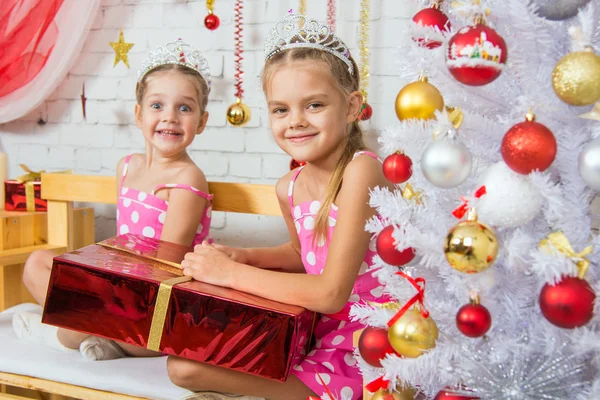 Two happy girls sitting on a bench with a Christmas present — ストック写真