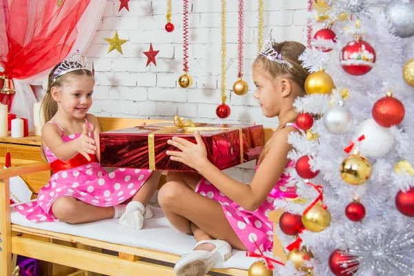 Girl gives a big red Christmas gift another girl sitting on the bench — ストック写真