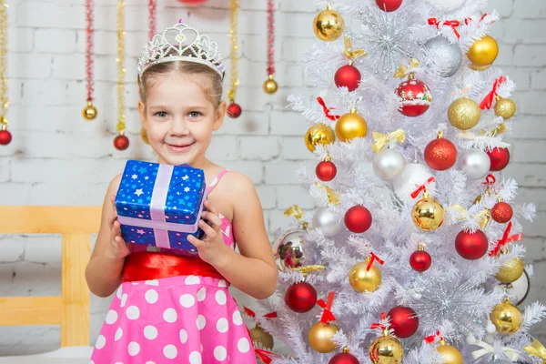 Niña feliz sosteniendo un regalo de Navidad y de pie cerca de los árboles de Navidad — Foto de Stock