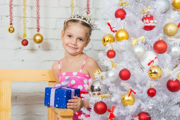 A girl stands at a Christmas fir-tree with gift in hand — ストック写真