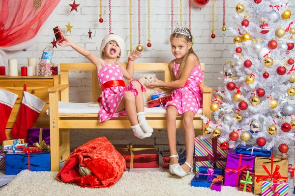 A girl enjoys the present, the other girl stroking a cat in a homelike atmosphere of the New Year — Stock Photo, Image