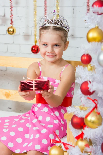 Four-year girl stretches forward a little gift sitting snowy Christmas trees Stockafbeelding