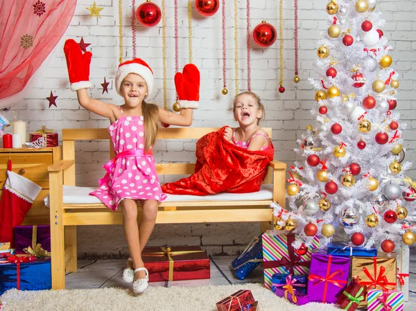 En el banco se sienta una chica en una gorra y mitones de Santa Claus, la otra chica con una risa sale de la bolsa — Foto de Stock