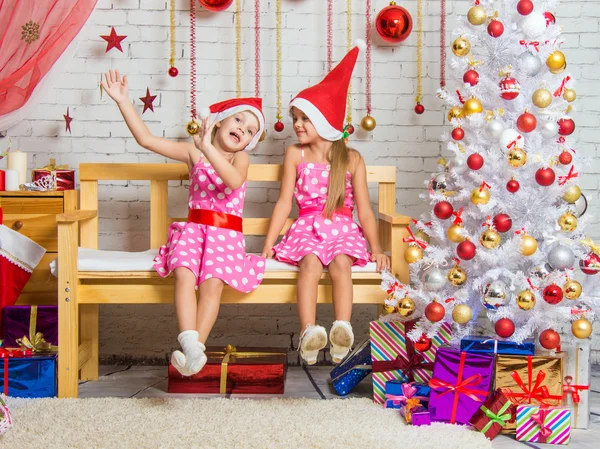 Dos chicas graciosas tontean sentadas en un banco en un entorno navideño — Foto de Stock