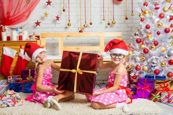Две забавные девушки держат большой подарок, сидя на ковре — стоковое фото