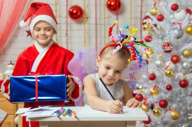Girl sits at a table with fireworks on the head, Santa Claus is preparing to surprise her