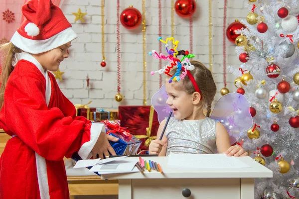 Chica se sienta en una mesa con fuegos artificiales en la cabeza, Santa Claus le dio un regalo —  Fotos de Stock