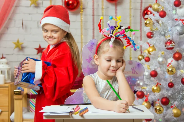 Chica se sienta en una mesa con fuegos artificiales en la cabeza, Santa Claus trae su regalo de Navidad —  Fotos de Stock
