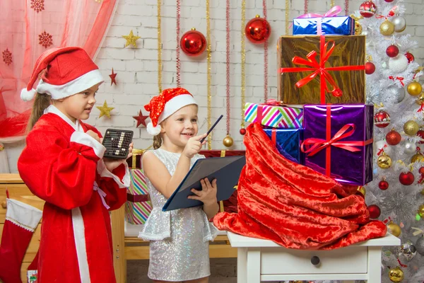 Santa y ayudante relatan felizmente los regalos en una bolsa y los comparan con la lista —  Fotos de Stock