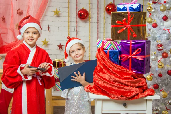 Santa Claus and assistant draw up a list of gifts and find them — Stockfoto