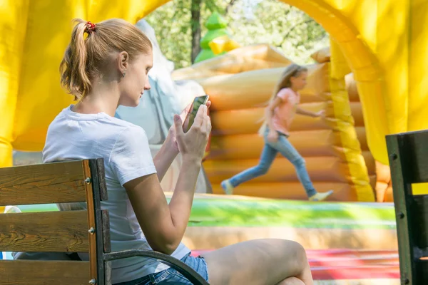 Young mother with a child at the phone waiting inflatable trampolines — Stock Photo, Image