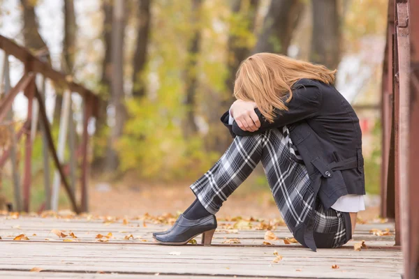 Triest meisje, zittend op een brug met haar hoofd rustend op zijn knieën — Stockfoto
