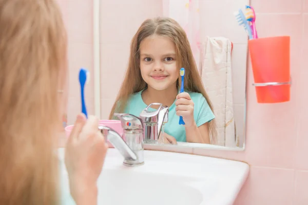 Zes jaar oud meisje en haar mond openen behandelt tanden in reflectie in een spiegel, terwijl in de badkamer — Stockfoto