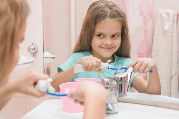 Happy little girl squeezes the toothpaste from a tube on toothbrush — Stok fotoğraf