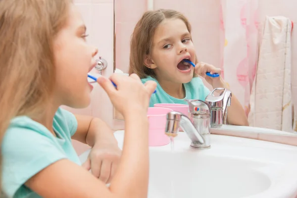 Sześć lat, który czyści dziewczynkę dolnych zębów bocznych spojrzeć w lustro w łazience — Zdjęcie stockowe