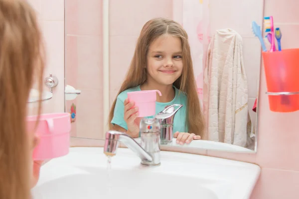 Chica feliz sosteniendo una taza y se mira en el espejo en el baño —  Fotos de Stock