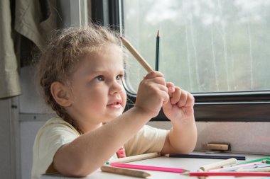 Girl looks funny on pencils at the table in the second-class train carriage