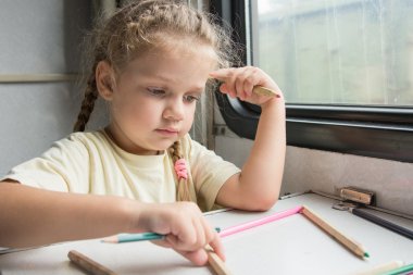 Four-year girl playing with pencils reserved seats at a table in a train