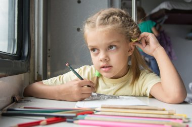 Six year old girl lost in thought looked out the window drawing pencils in second-class train carriage