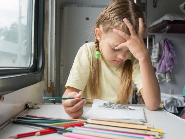Six year old girl thoughtfully draws pencils in second-class train carriage