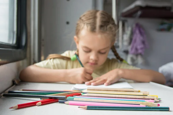 Lápices en primer plano, en el fondo una niña de seis años dibujando lápices en un vagón de tren de segunda clase — Foto de Stock