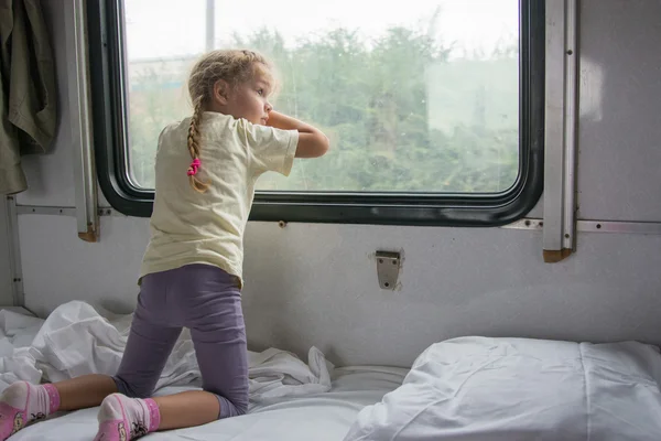 Четырехлетняя девочка на полке поезда смотрит в окно — стоковое фото
