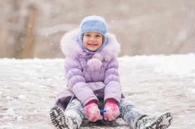 Joyful five years girl rolls down from the icy hill