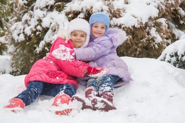 Two girls are sitting in a snowdrift snow and hugging each other — Stock Photo, Image