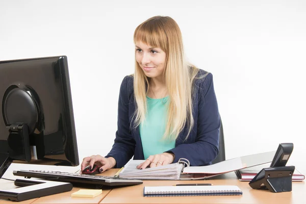Office employee working at the computer and a folder of paper documents — Stockfoto