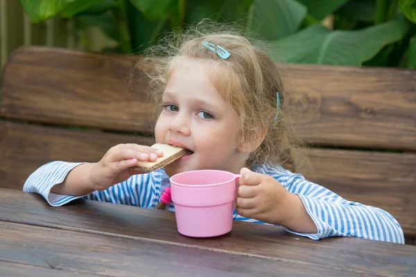 Четырехлетняя девочка кусает вафли и пьет чай. — стоковое фото