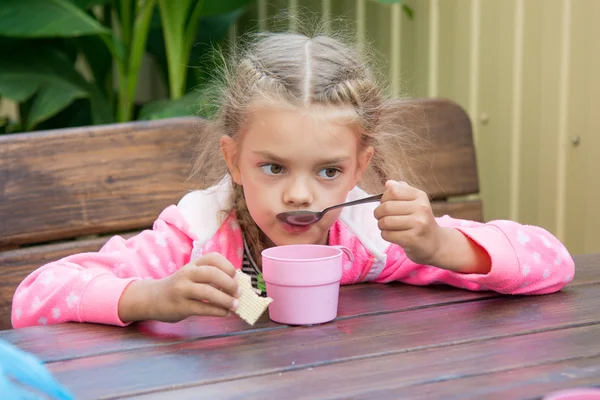 Menina de seis anos bebe chá de uma colher de café da manhã na varanda — Fotografia de Stock