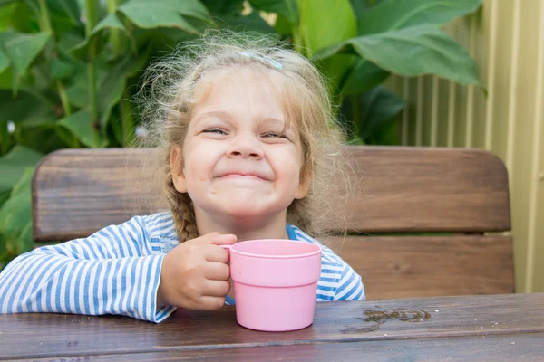 Fille de quatre ans martelant assis à une table avec un verre de jus — Photo