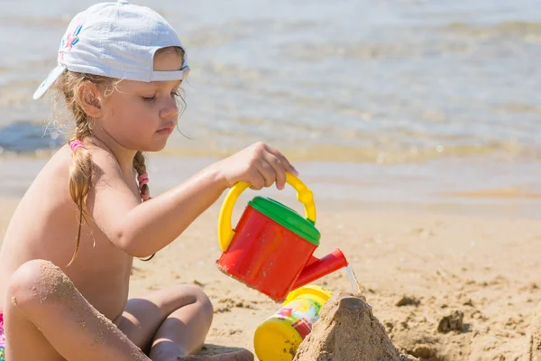 Четырехлетняя девочка льет воду на песочный замок — стоковое фото